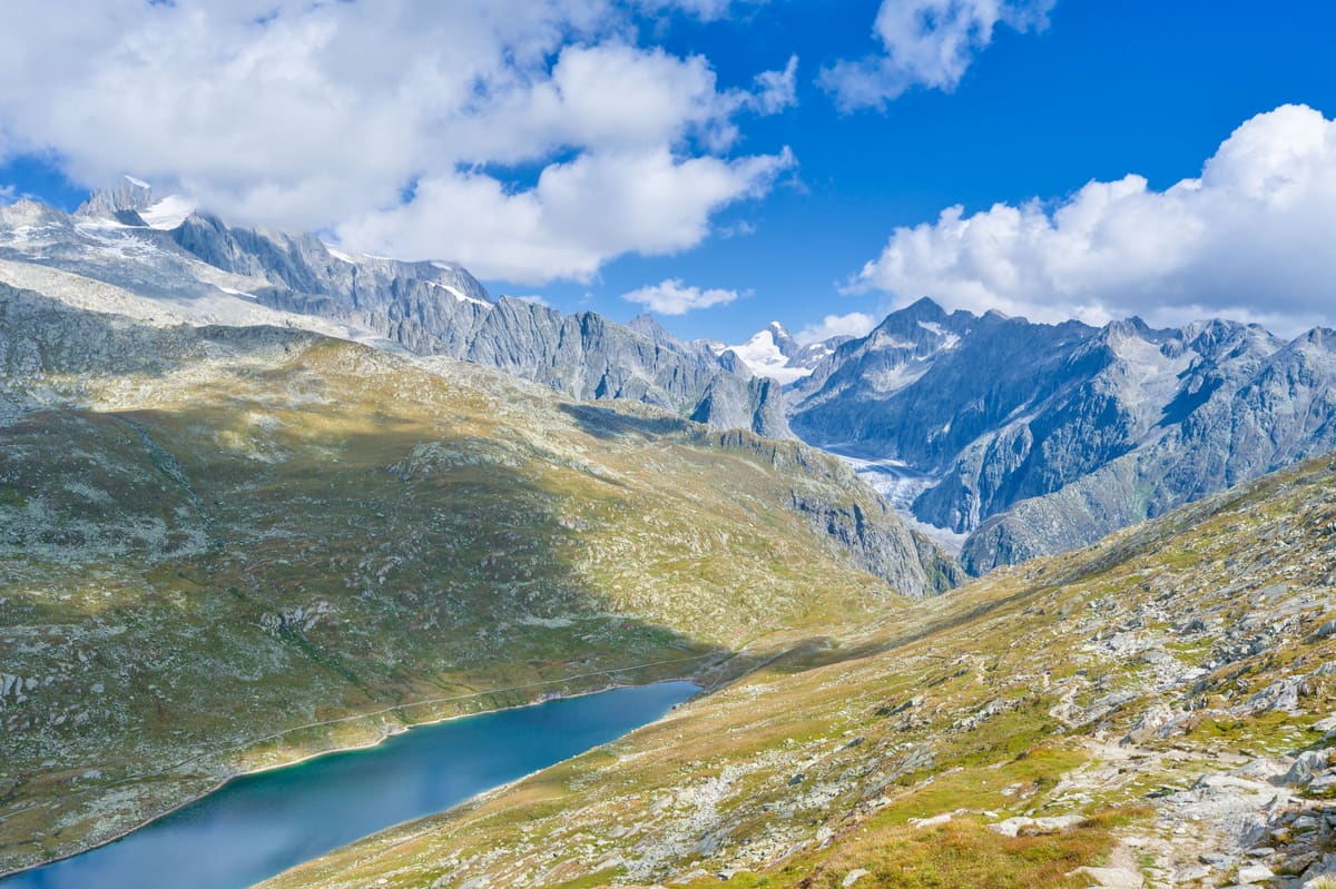 A breathtaking view of the Swiss Alps with a tranquil lake and rugged mountain peaks under a vibrant sky.